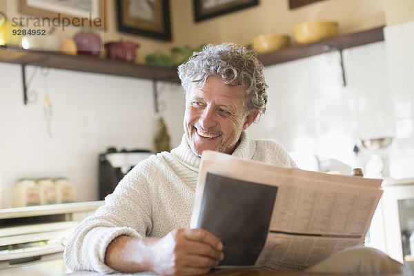 Älterer Mann liest Zeitung in der Küche