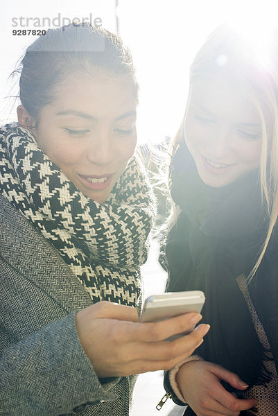 Junge Frauen im Freien schauen gemeinsam aufs Handy