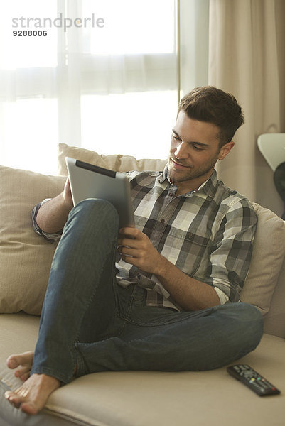 Junger Mann entspannt auf der Couch zu Hause mit digitalem Tablett