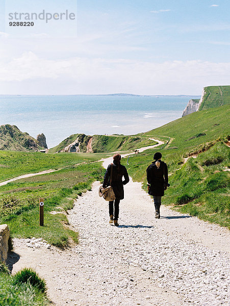 Zwei Frauen gehen auf einem Küstenwanderweg entlang von Klippen.