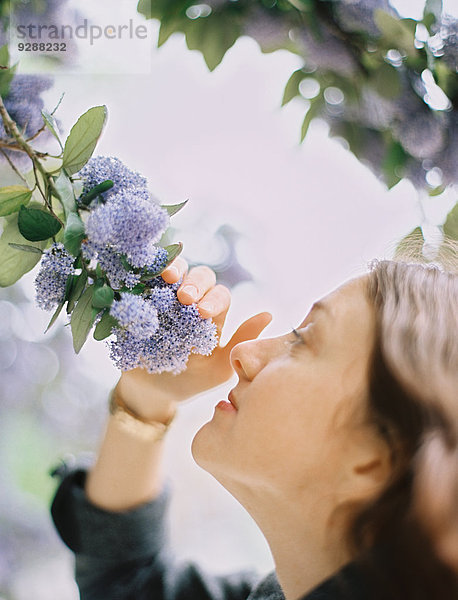 Eine Frau zieht blaue Blumen zu sich heran  um den Duft einzuatmen.