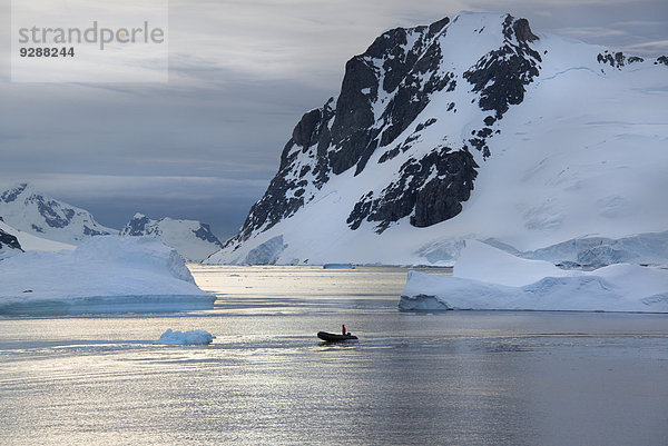 Menschen in kleinen aufblasbaren Zodiac-Rib-Booten  die auf dem ruhigen Wasser um kleine Inseln der Antarktischen Halbinsel an Eisbergen und Eisschollen vorbeifahren.
