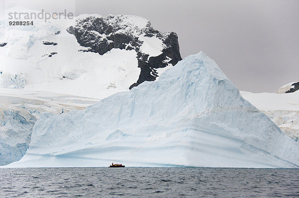 Menschen in kleinen aufblasbaren Zodiac-Rib-Booten  die auf dem ruhigen Wasser um kleine Inseln in der Antarktis an Eisbergen und Eisschollen vorbeifahren.