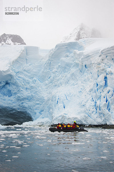 Menschen in kleinen aufblasbaren Zodiac-Rib-Booten  die auf dem ruhigen Wasser um kleine Inseln in der Antarktis an Eisbergen und Eisschollen vorbeifahren.