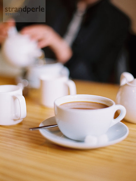 Eine sitzende Frau gießt aus einer Teekanne aus weißem Porzellan eine Tasse Tee aus.