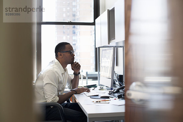 Ein Mann  der in einem Büro arbeitet und an einem Schreibtisch sitzt. Er schaut auf einen Computerbildschirm.