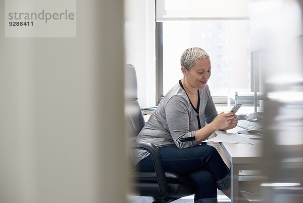 Eine Frau  die allein in einem Büro arbeitet und ihr Smartphone überprüft.