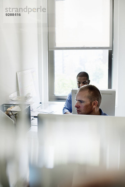 Zwei Männer arbeiten in einem Büro und benutzen Computer.