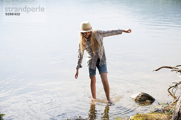 Ein Mädchen mit Strohhut paddelt im seichten Wasser eines Bergsees.