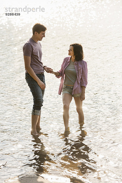 Ein Paar hält sich an den Händen und paddelt im flachen Wasser am See.