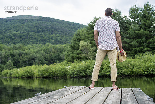 Ein Mann steht auf einem Holzsteg mit Blick auf einen ruhigen See.