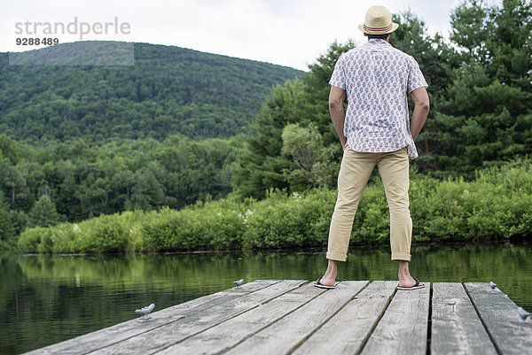 Ein Mann steht auf einem Holzsteg mit Blick auf einen ruhigen See.