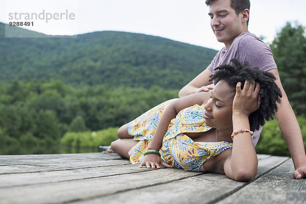 Ein Paar entspannt sich auf einem Steg mit Blick auf einen Bergsee.
