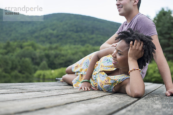 Ein Paar entspannt sich auf einem Steg mit Blick auf einen Bergsee.