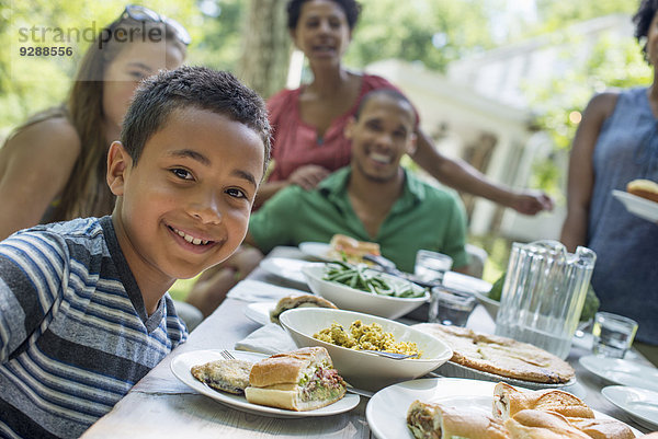 Ein Familientreffen  Männer  Frauen und Kinder um einen Tisch in einem Garten im Sommer. Im Vordergrund ein lächelnder Junge.