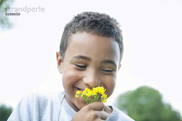 Junge lächelt und hält Blume.