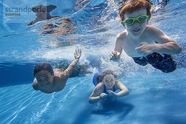 Drei Kinder schwimmen unter Wasser und lächeln dabei in die Kamera.