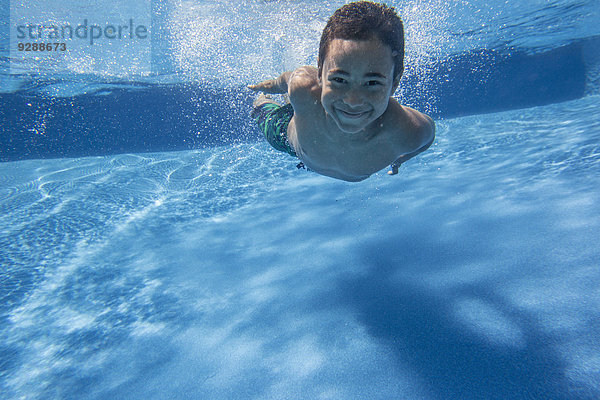 Ein Junge schwimmt unter Wasser und lächelt in die Kamera.