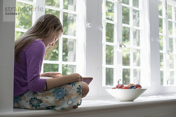 Mädchen  das am Fenster sitzt und ein Buch liest.