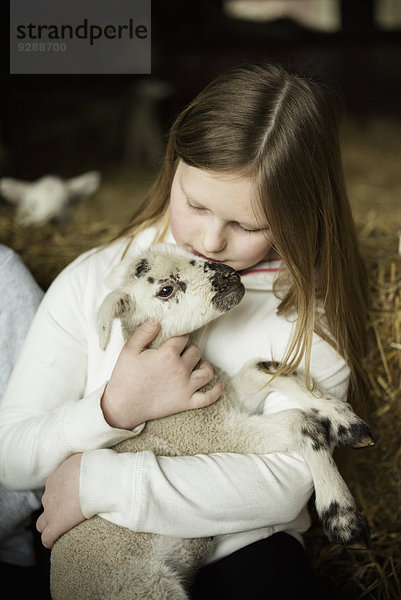 Ein Mädchen  das ein kleines neugeborenes Lamm hält.