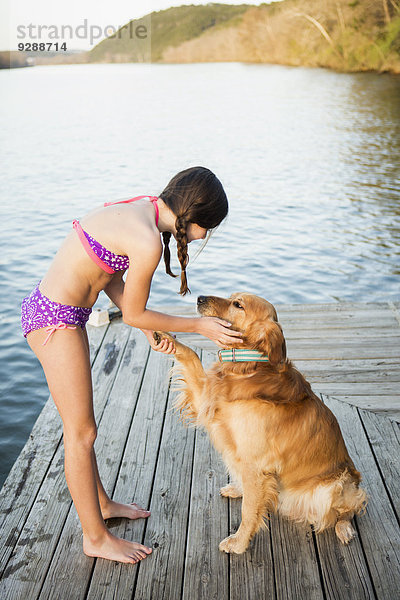 Ein Mädchen im Bikini mit einem Golden Retriever Hund  der die Pfote hochhebt.