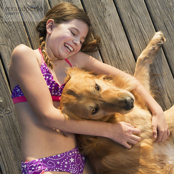 Ein Mädchen im Bikini neben einem Golden-Retriever-Hund liegend  von oben betrachtet.