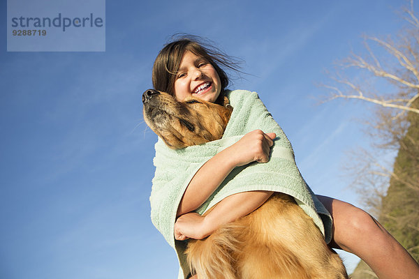 Ein Mädchen in einem Strandtuch mit einem Golden-Retriever-Hund.