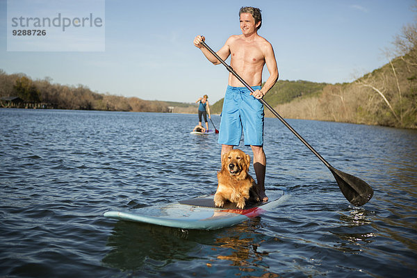 Ein Mann steht mit einem Hund auf einem Paddelbrett.