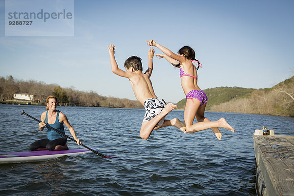Zwei Kinder springen von einem Steg ins Wasser.