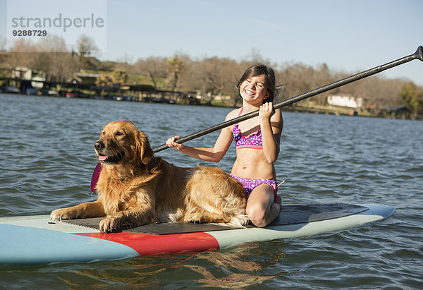 Ein Kind und ein Apportierhund auf einem Paddelbrett auf dem Wasser.