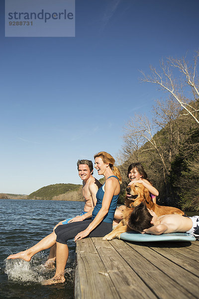 Eine Familie und ihr Apportierhund auf einem Steg an einem See.
