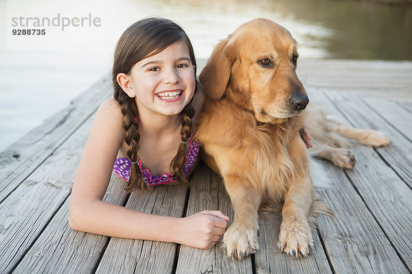 Ein junges Mädchen und ein Golden Retriever Hund liegen auf einem Steg.