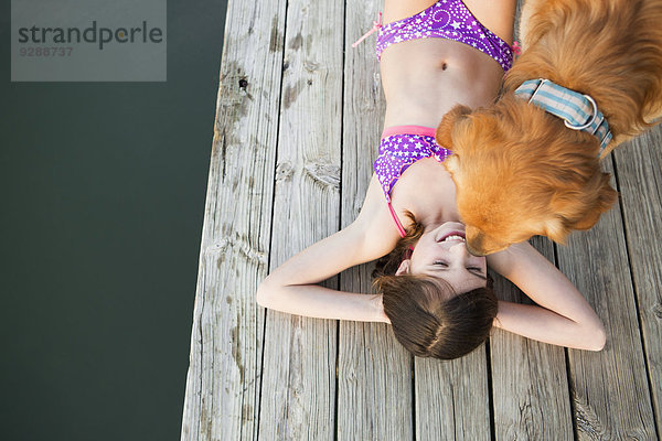 Ein junges Mädchen und ein Golden Retriever Hund auf einem Steg.