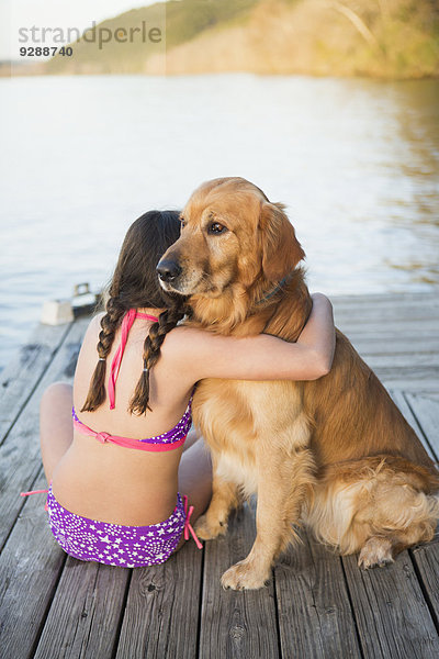 Ein junges Mädchen und ein Golden Retriever Hund sitzen auf einem Steg.