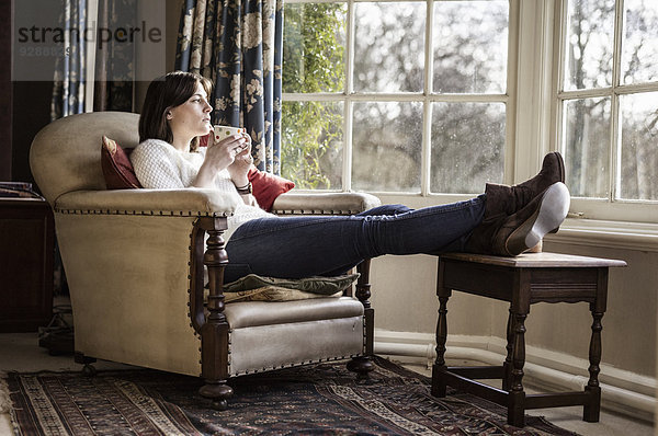 Eine junge Frau  die sich zu Hause entspannt  die Füße hochgelegt und eine Tasse Tee trinkt.