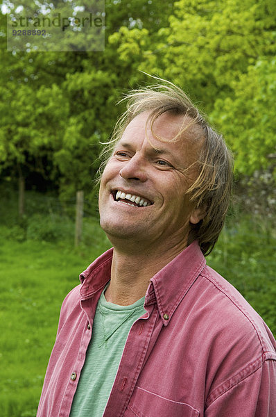 Ein reifer Mann in legerer Kleidung mit blonden Haaren  breit lächelnd.