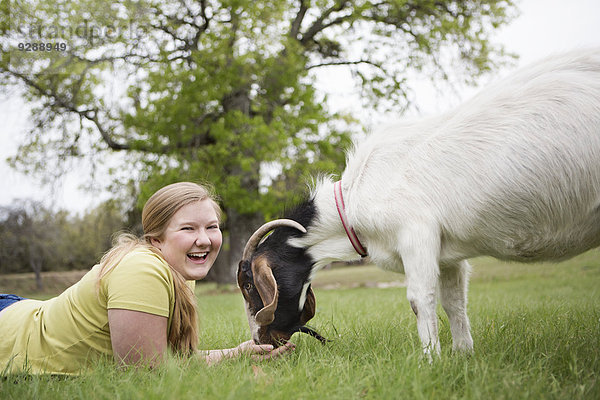 Ein Mädchen  das Kopf an Kopf mit einer Ziege auf Gras liegt.