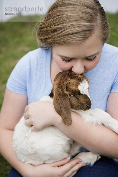 Ein Mädchen kuschelt ein Ziegenbaby.