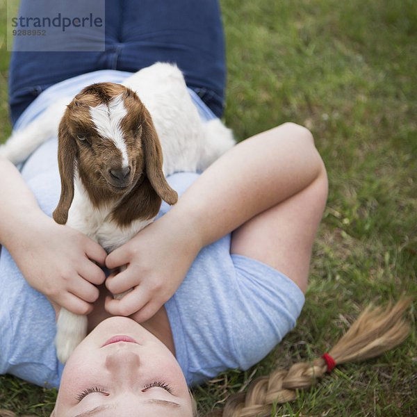 Ein Mädchen kuschelt ein Ziegenbaby  das auf ihrer Brust liegt.