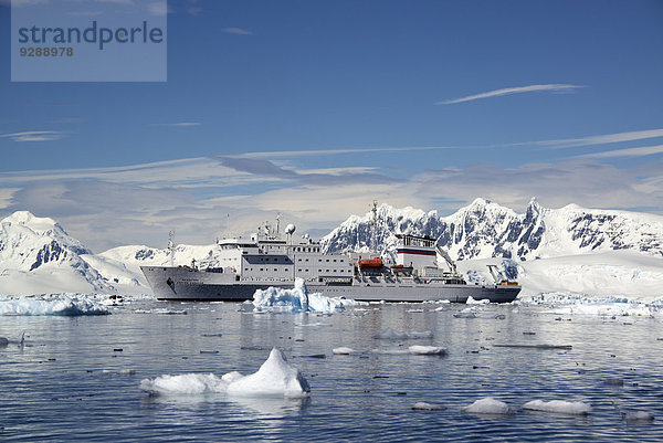 Ein antarktisches Kreuzfahrtschiff mit aufblasbaren Zodiacs auf dem ruhigen Wasser zwischen Eisschollen und Gebirgslandschaft.