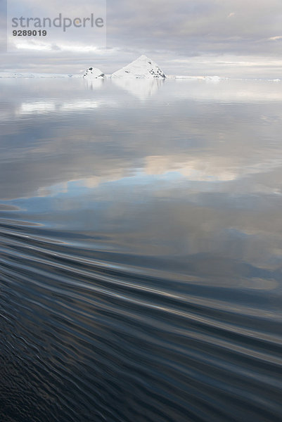 Schneebedeckte Berge  die sich im ruhigen Wasser des Ozeans spiegeln.