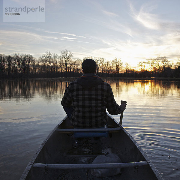 Ein Mann im Kanu auf einem See bei Sonnenuntergang  Rückansicht