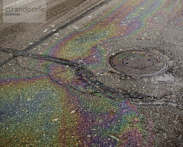 Öl auf einer nassen  gerissenen Straße in der Nähe eines Schachtes