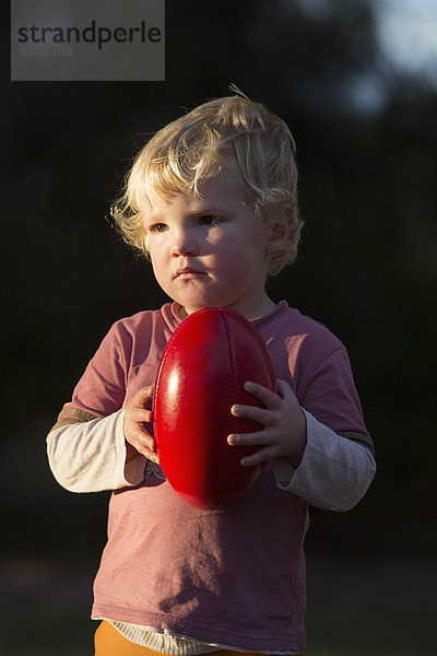 Süßer Junge schaut weg  während er draußen einen Fußball hält.