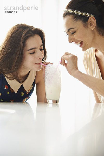 Mutter und Tochter blasen Blasen in Milch zusammen am Tisch