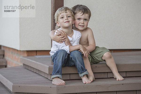 Ganzflächiges Porträt von Jungen  die auf der Veranda sitzen