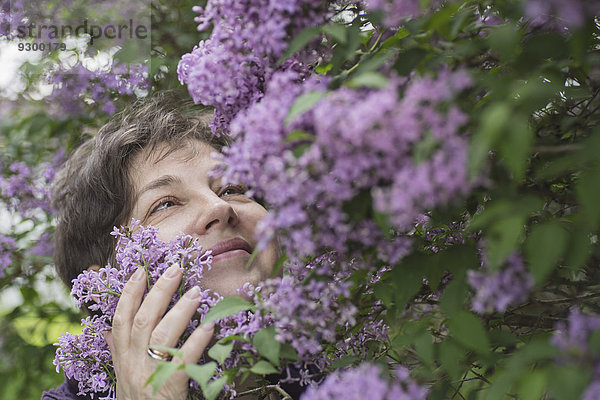 Fröhliche reife Frau  die blühende Blumen im Park betrachtet.