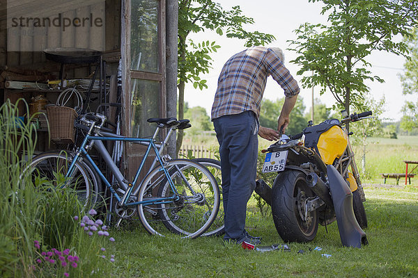 Rückansicht des reifen Mannes  der das Motorrad auf dem Hof repariert.