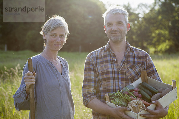 Porträt eines reifen Paares mit einer Kiste frisch geernteten Gemüses im Garten