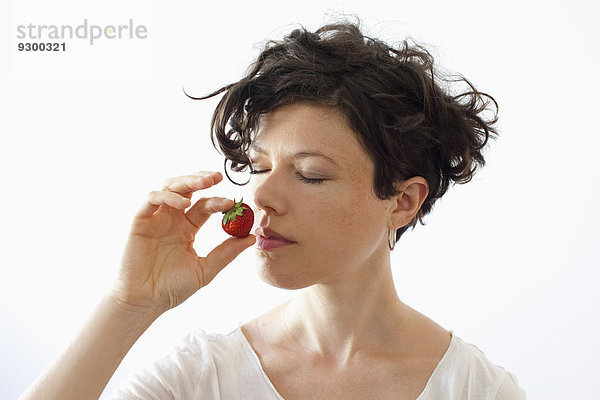 Eine Frau  die Erdbeere auf weißem Hintergrund riecht.